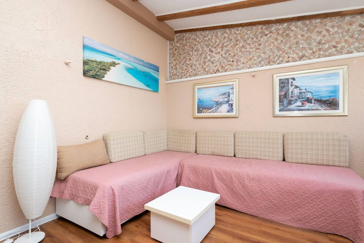 Una stanza con un divano color beige, un comodino bianco e un ventilatore a muro.
