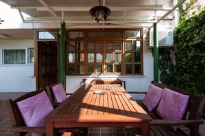 Une table en bois, quatre chaises, un ventilateur de plafond et une fenêtre donnant sur un paysage verdoyant.