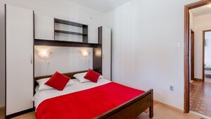 Une chambre à coucher avec un lit, une literie rouge, une armoire et une étagère intégrée.