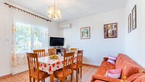 Un coin repas avec une table dressée pour quatre personnes, un téléviseur fixé au mur et un canapé avec des coussins.