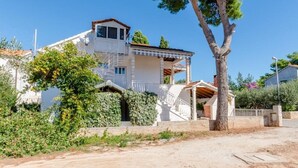 Une maison à deux étages avec un balcon, entourée de verdure et d’un arbre.