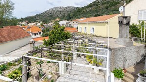 Ein Dachgarten mit einer Pergola, Kübelpflanzen und einem Steingebäude.