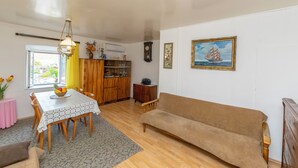 Ein gemütliches Wohnzimmer mit Holzboden, einem beigen Sofa, einem Esstisch mit Stühlen, einer Küchenzeile mit Schränken und einem Bild eines Segelbootes an der Wand.