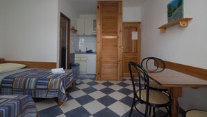 Una stanza con due letti, un tavolo di legno, una sedia, un angolo cottura e una porta che dà su un'altra stanza.