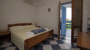 Una camera da letto con un letto in legno, un comodino, un tavolino e una porta che dà su un balcone esterno.