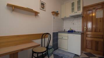 A compact kitchen with a wooden bench, a chair, a sink, and a cabinet.