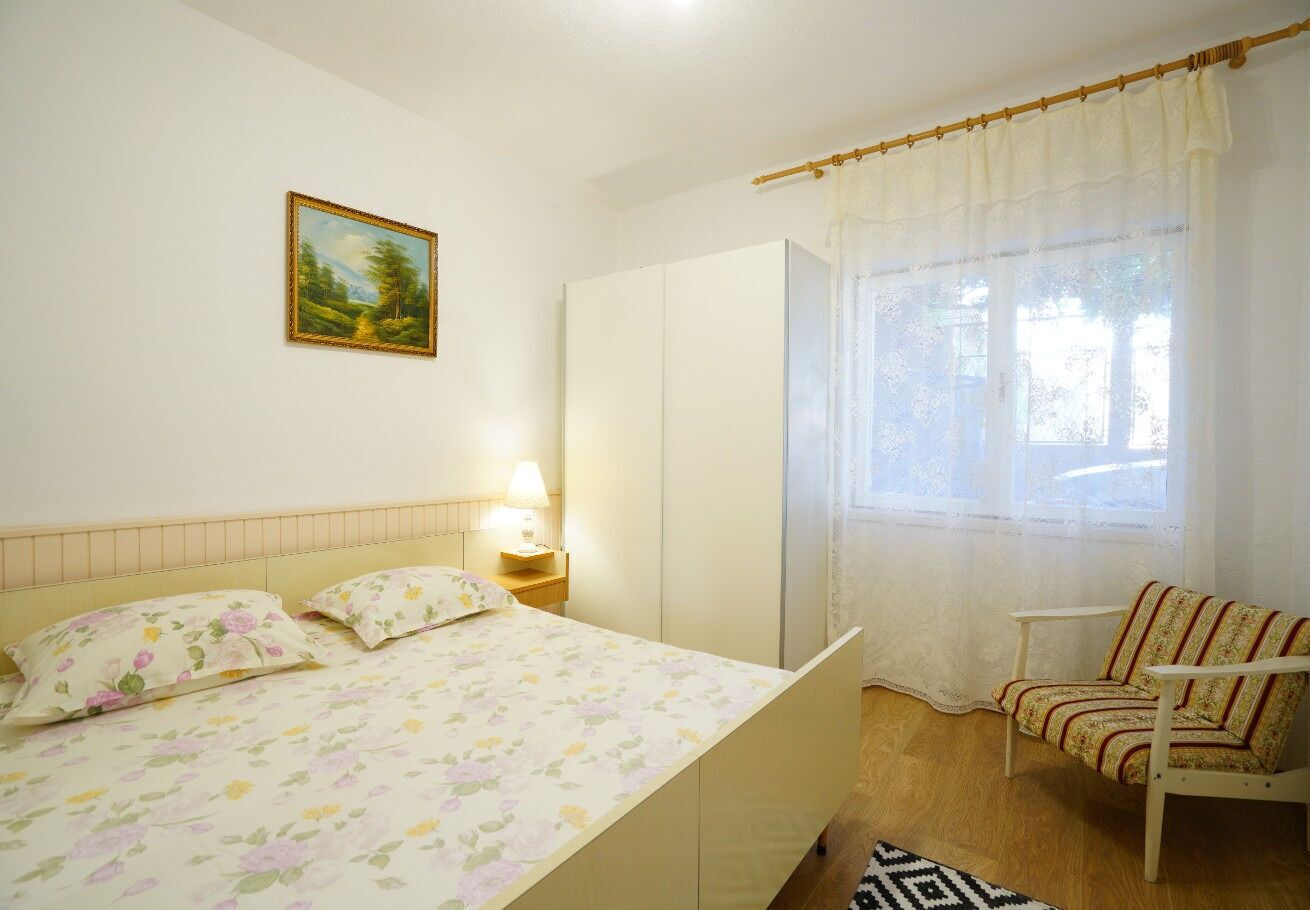 A bedroom with a bed, a chair, a wardrobe, a painting, and a window with curtains.