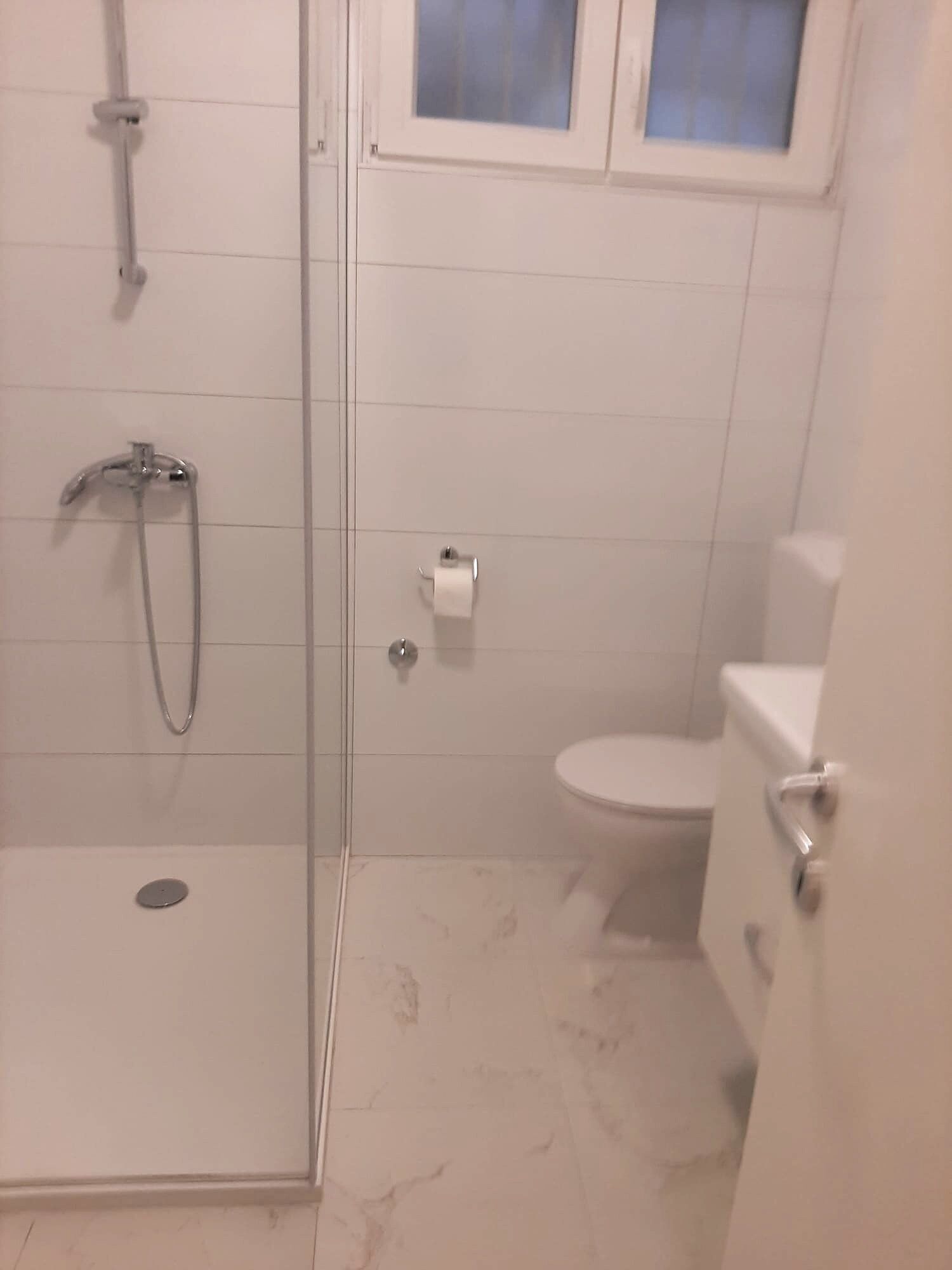 Et badeværelse med et glasafskærmet brusebad, toilet og et vindue over toilettet.