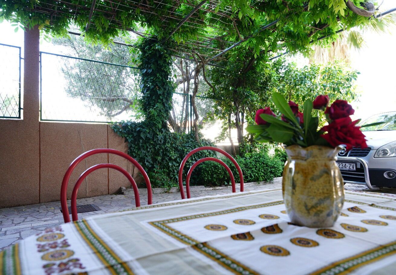 An outdoor table with a patterned tablecloth, a vase with red flowers, and red chairs.