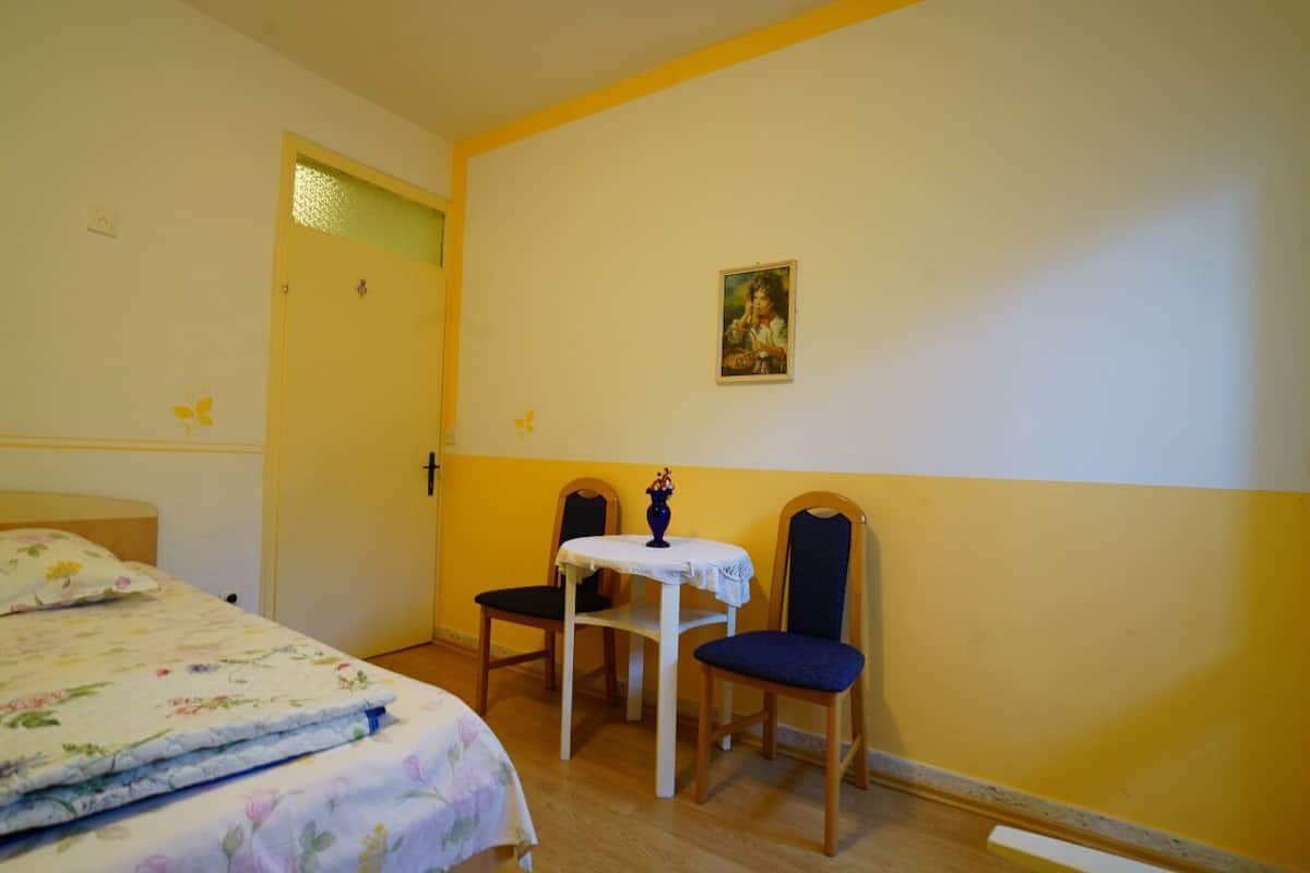 Ett rum med en säng, ett litet bord med stolar och en tavla på väggen.