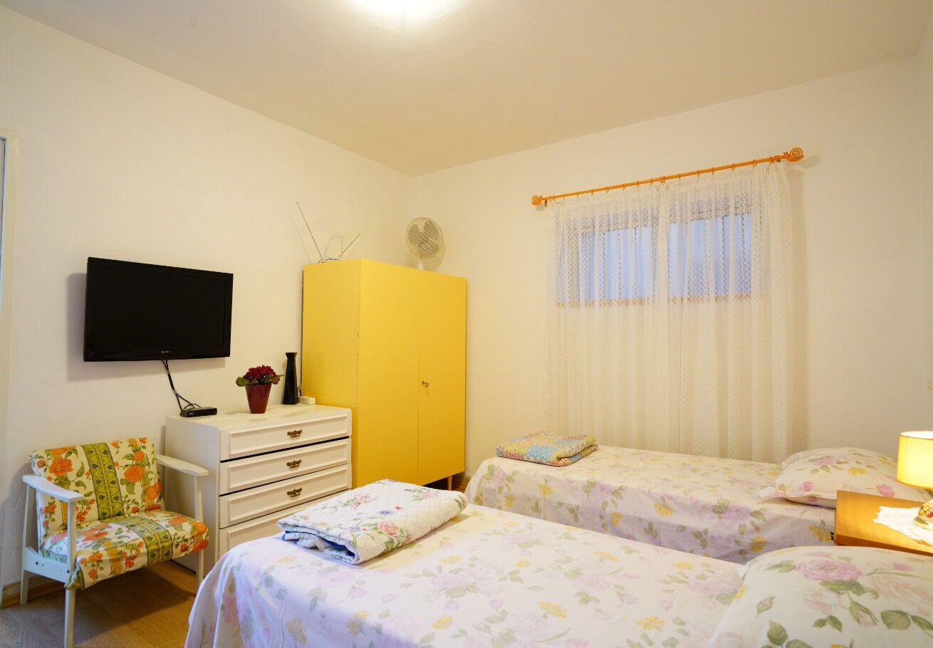 Un dormitorio con dos camas, un televisor, un armario amarillo, una silla y una ventana con cortinas.