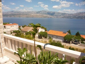 A balcony with a view of a coastal town, a body of water, and mountains in the distance. - Apartment Juri (Postira)