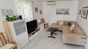 En kompakt opholdsstue med sofa, fjernsyn, lille bord, stol og et skab med et fladskærms-TV.