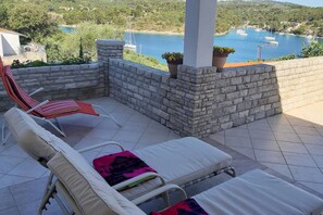 Un patio con dos sillones de descanso y una mesita, con vista a una bahía pintoresca con barcos.
