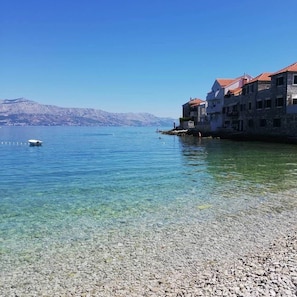 A coastal area with clear water, pebbly beach, and stone buildings with red roofs. - Apartments Zana (Postira)