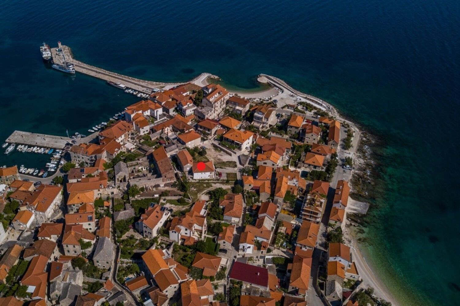 An aerial view of a coastal town with a marina, dense housing, and a prominent curved road.