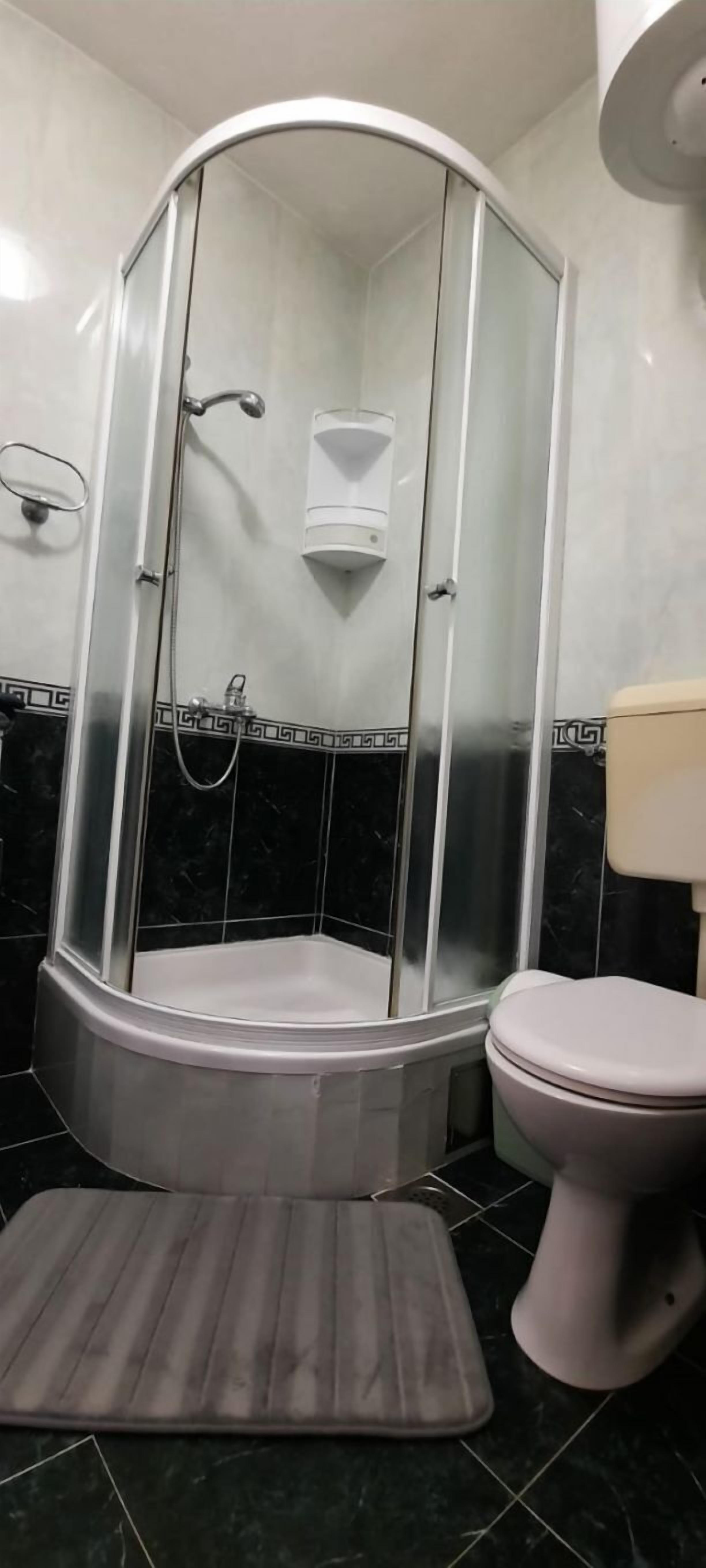 A bathroom with a glass-enclosed shower, a toilet, and a marble-tiled floor.