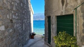 En smal gata med hus byggda av sten, en krukväxt och utsikt över havet.