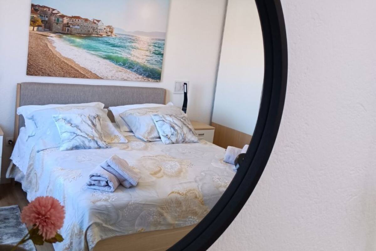 Un dormitorio con cama, almohadas, una mesita de noche, un cuadro enmarcado en la pared y un espejo.