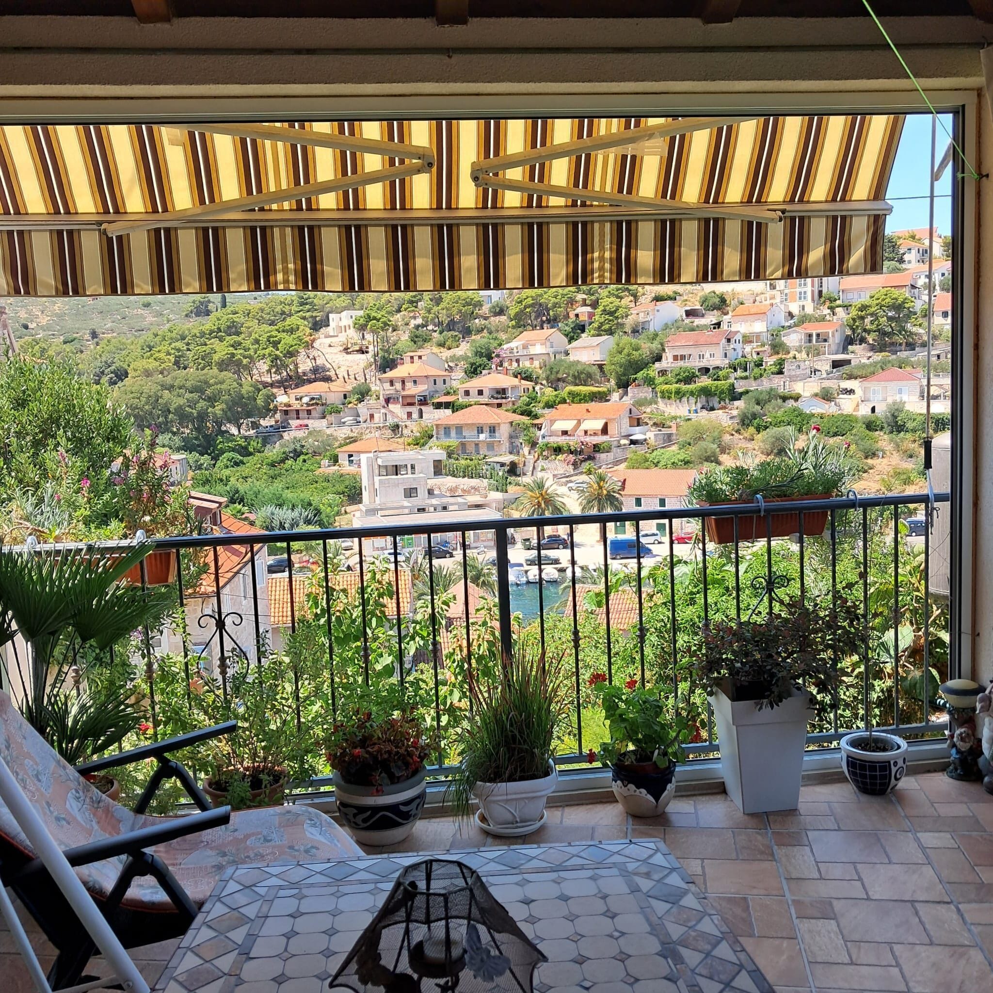 A balcony with a view of a hillside town, potted plants, and a tiled floor.