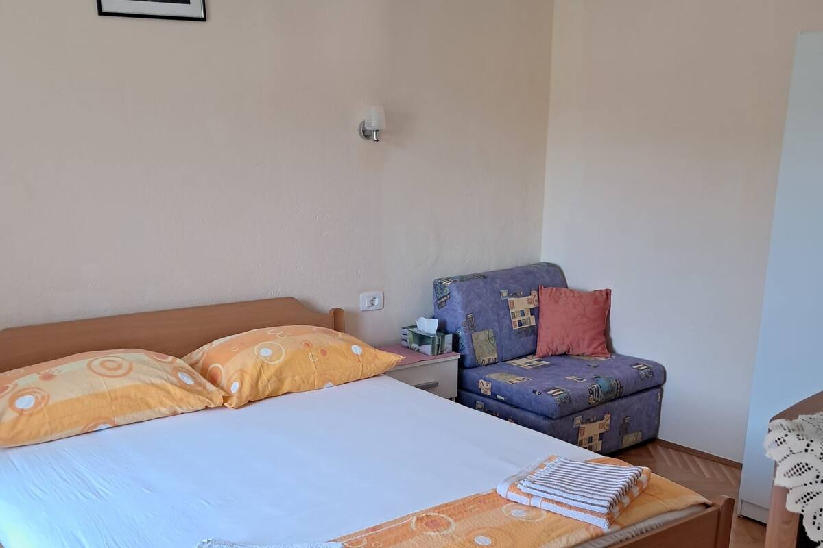 A neatly made bed with a white and orange bedspread, a wooden headboard, and a small bedside table with a lamp.