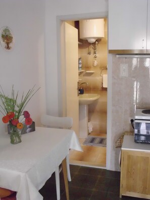 A small kitchen with a white table and chairs, a wooden cabinet, and a vase with flowers on the table. - Apartments Kat (Supetar)