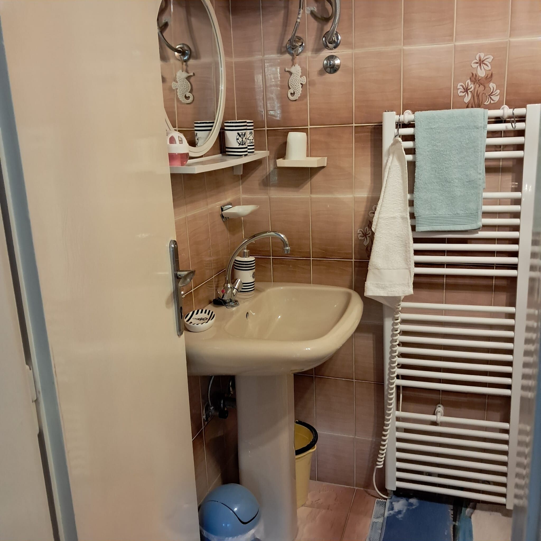 Un baño con lavamanos, espejo, toallero y un estante pequeño con artículos de aseo.