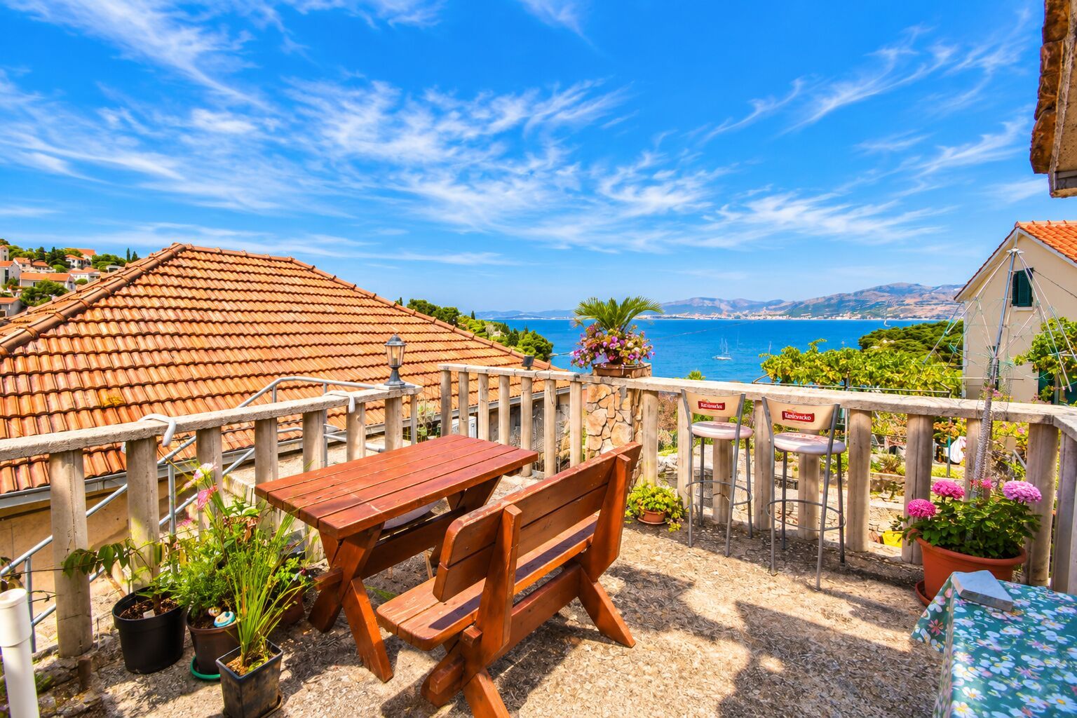 A terrace with a wooden table and chairs, potted plants, and a view of the sea.