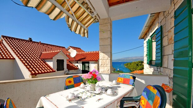 A balcony with a table set for dining, chairs, and a view of the sea. - Apartments Kat (Supetar)
