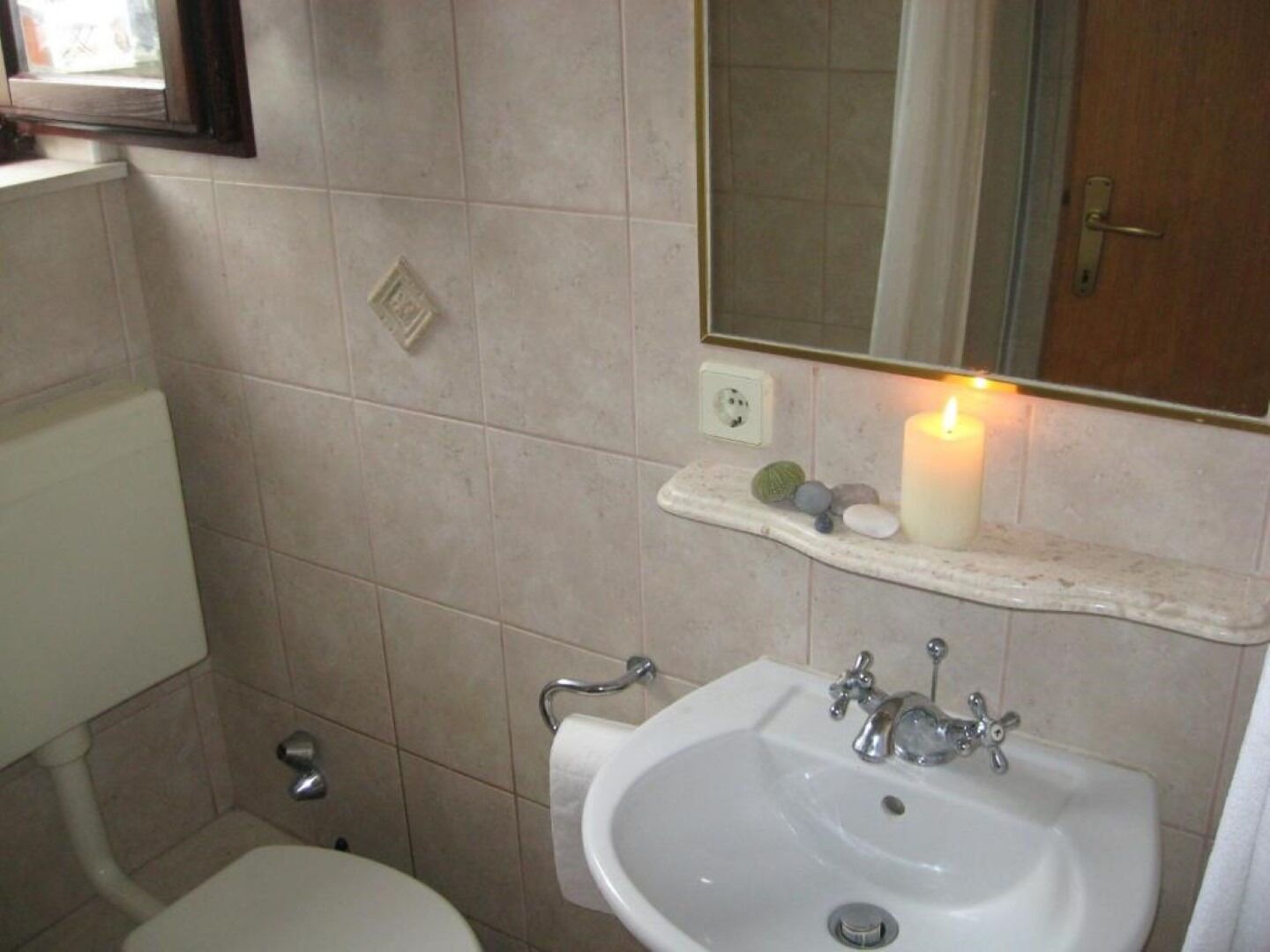 Un bany amb un lavabo blanc, un mirall a sobre i una petita estant amb una espelma i pedres.