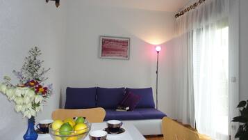 Un comedor con una mesa preparada para dos personas, un florero con flores y un sofá al fondo.