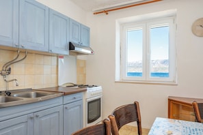 A kitchen with a stove, sink, and window overlooking a body of water. - Apartments Sova (Postira)