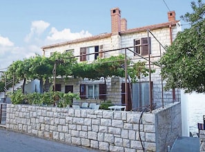 A stone building with a tiled roof, a stone wall in front, and a pergola with vines. - Apartments Sova (Postira)