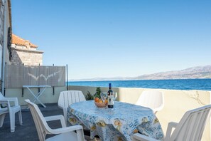 A terrace with a table set for two, overlooking a body of water and distant mountains. - Apartments Sova (Postira)
