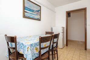 A dining area with a table, chairs, and a refrigerator. - Apartments Sova (Postira)