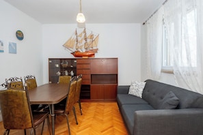 A dining area with a wooden table and chairs, a built-in wooden cabinet, and a ship model above the cabinet. - Apartments Sova (Postira)