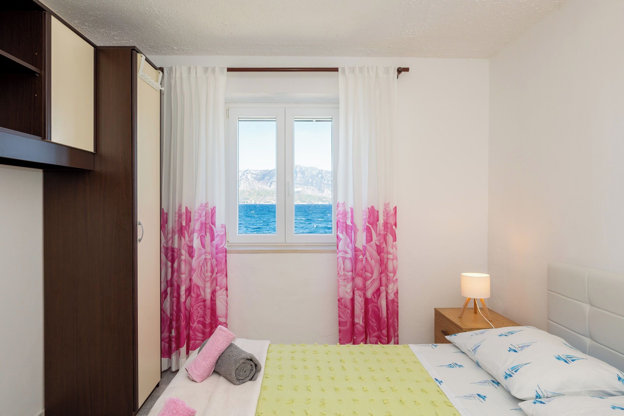 A bedroom with a bed, a nightstand, a lamp, and a window with curtains.
