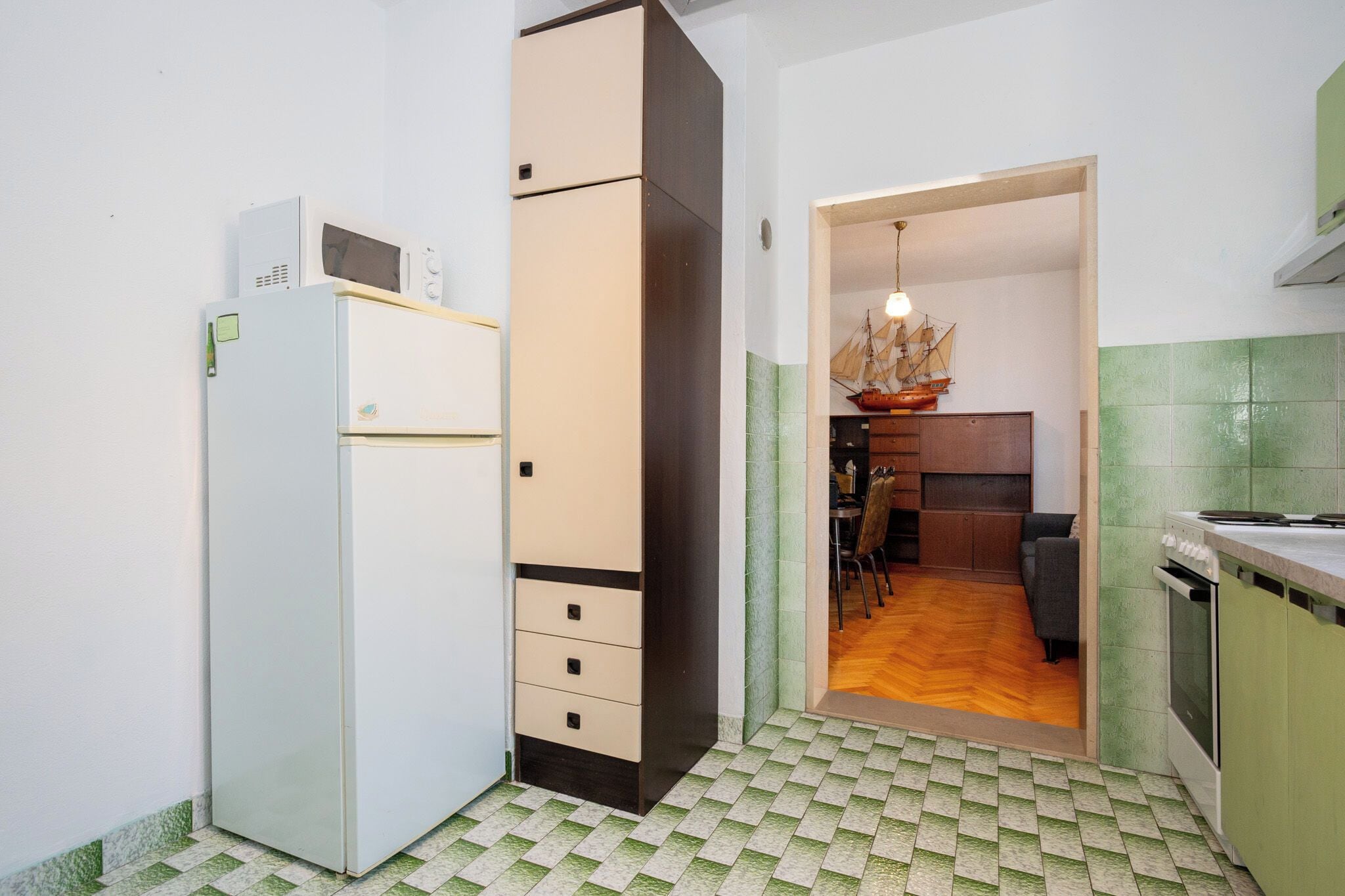 Cozinha compacta com geladeira, armários e espaço de refeições com cadeira e mesa.