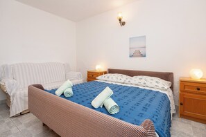 A bedroom with a bed, a sofa, a nightstand, and a wall-mounted light fixture. - Apartments Sova (Postira)