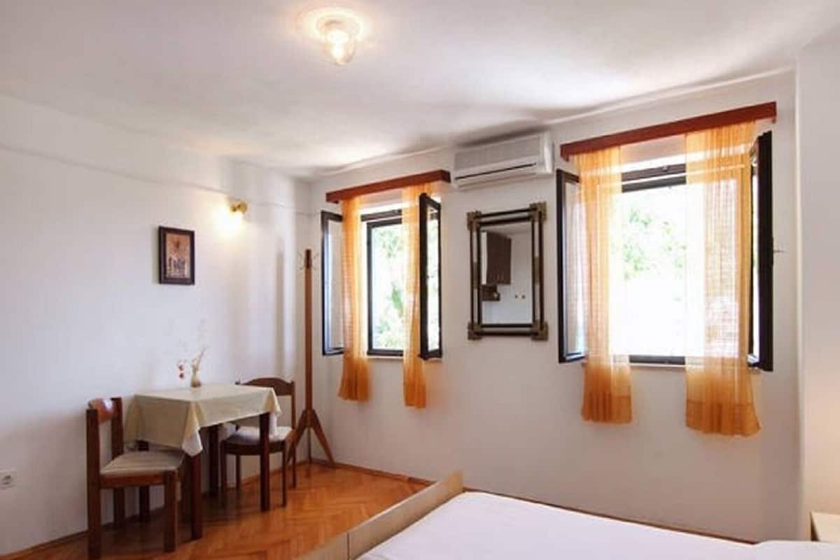 A room with a bed, a table with chairs, and two windows with curtains.