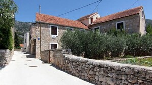 Un vicolo stretto con edifici in pietra, un muro di pietra e vegetazione.