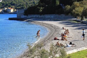 Una playa de guijarros con gente tomando el sol y nadando.