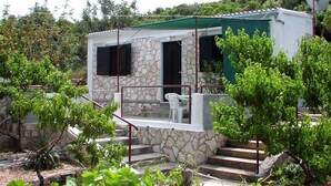 A small stone building with a green roof, a porch with a white chair, and steps leading up to the entrance. - House Paulo1 (Vis)