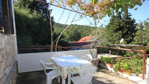 A patio with a table and chairs, surrounded by potted plants and a view of a house and trees. - House Paulo1 (Vis)