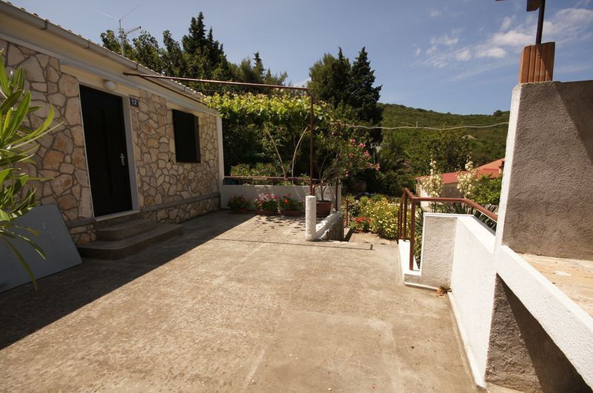A stone building with a door and window, a concrete patio, and a garden with plants and flowers.