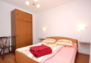 A bedroom with a bed, a wooden wardrobe, a chair, and two wall-mounted lamps. - Apartments Roki (Vis)