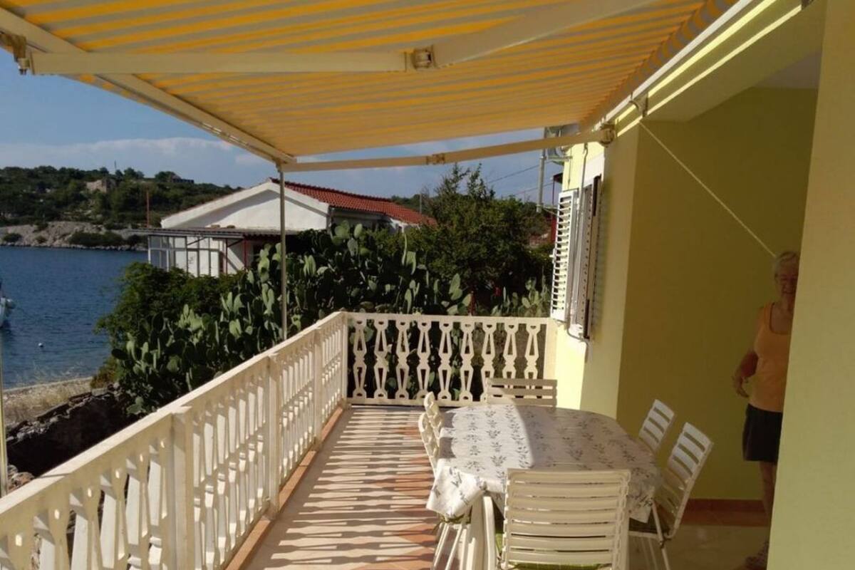 A covered outdoor patio with a table and chairs, a railing, and a view of the sea.