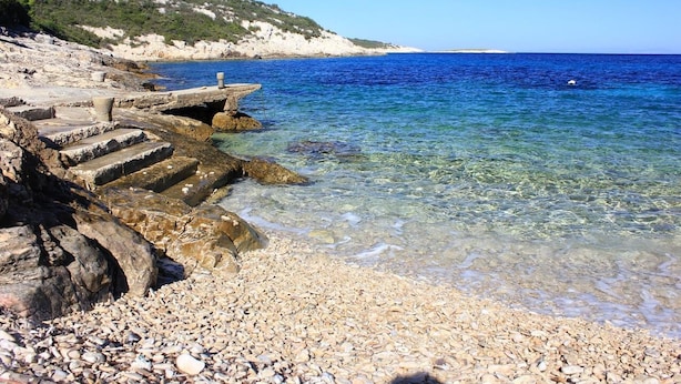 Ein felsiger Strand mit klarem, blauem Wasser und einer Steintreppe, die ins Meer führt.