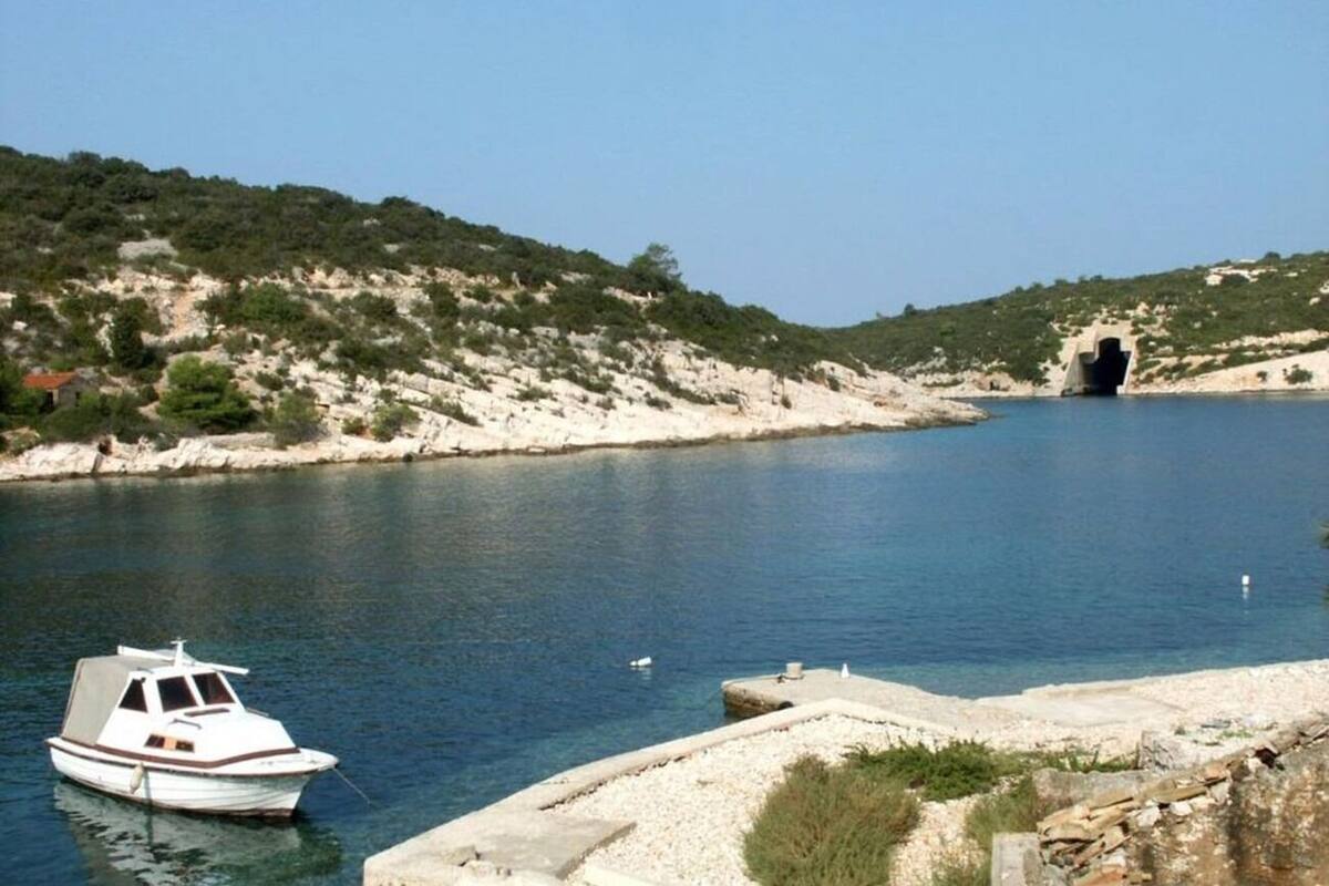 A boat docked near a rocky shoreline with a tunnel entrance in the background.