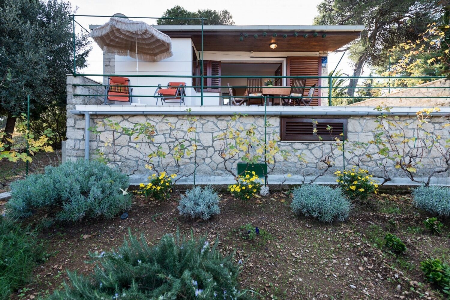 A modern house with a stone facade, outdoor seating, and a garden with various plants.